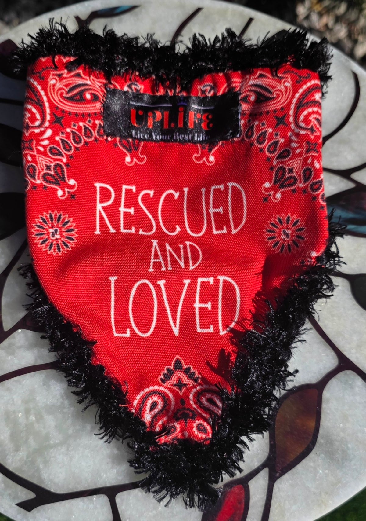 Rescued and Loved Dog Bandana, flat front view showing red paisley print, Rescued and Loved lettering and sewn-in UPLIFE label
